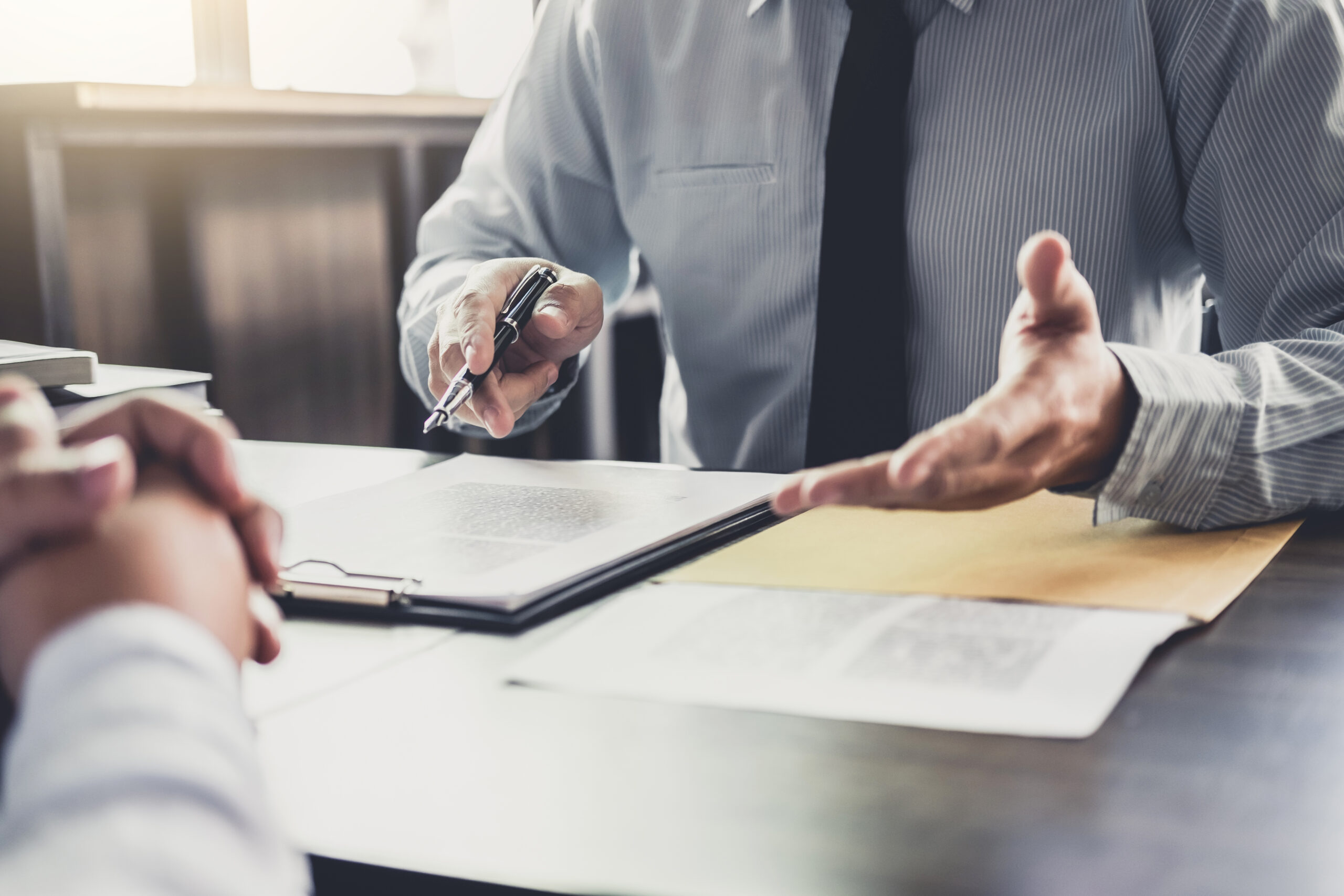 A business professional gestures while discussing documents with a client, emphasizing communication and decision-making in a meeting setting.