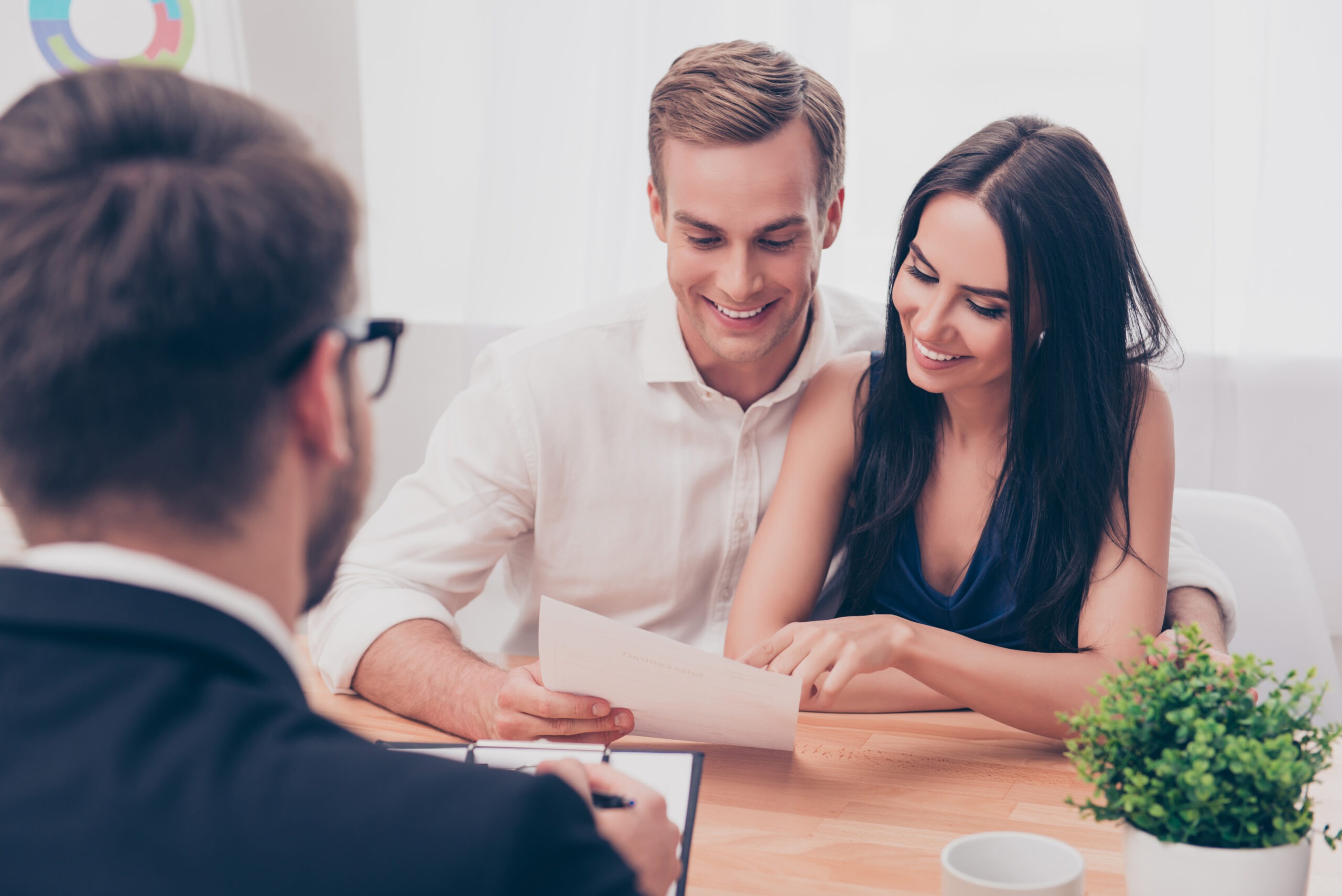A couple smiles while reviewing documents during a meeting with a professional, suggesting a discussion about financial planning or real estate.
